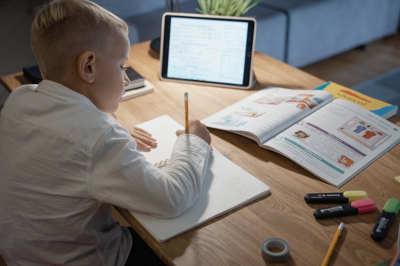 Boy working independently at his desk with notebook and tablet, comfortable home workspace for studying